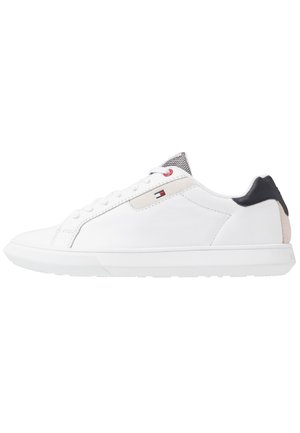 Baskets basses blanches avec lacets blancs, empiècement noir au talon, détail beige, et un petit logo de drapeau rouge, blanc et bleu sur le côté.