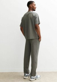 Conjunto gris a juego formado por una camiseta de manga corta y pantalones, confeccionado en tejido suave con un ajuste relajado. Las zapatillas complementan el conjunto.