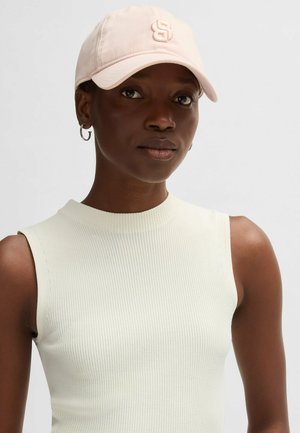 Rosa Baseball-Cap mit gesticktem Logo, aus Baumwollmaterial, mit gebogenem Schirm. Modell trägt ein ärmelloses, geripptes Top in hellcremefarbener Farbe.