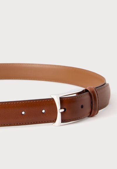 Ceinture en cuir marron avec boucle métallique argentée et couture visible, posée en boucle lâche sur un fond clair uni.