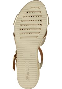 Sandalo oro e beige con suola in gomma testurizzata, dotato di scanalature e perforazioni per la traspirabilità, insieme a una cinghia regolabile.