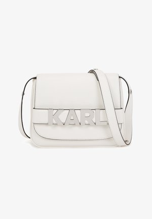 Weiße Leder-Schultertasche mit silbernen "KARL" Metallbuchstaben auf der vorderen Klappe und einem verstellbaren Tragegurt.
