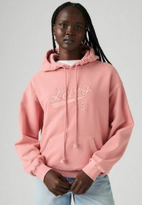 Sudadera rosa con capucha, que presenta un logo texturizado en blanco en el pecho, puños elásticos y un bolsillo tipo canguro en la parte frontal.