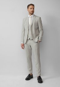 Un costume trois pièces gris clair avec une finition texturée, comprenant une veste ajustée, un pantalon slim et une chemise et cravate blanches contrastantes. Mocassins noirs.
