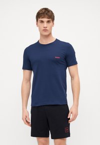 Navy blue cotton t-shirt with short sleeves and a round neck, featuring a small red "HUGO" logo on the left chest.