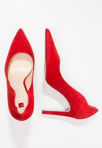 Tacchi alti rossi in suede con design a punta, lati aperti e un piccolo accento quadrato. Il tacco è in stile stiletto, aggiungendo altezza.