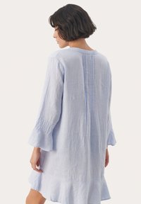 Rochie din in de culoare albastru deschis, cu mâneci clopot 3/4, tiv volant și detalii cu dungi verticale pe spate. Material moale și texturat.