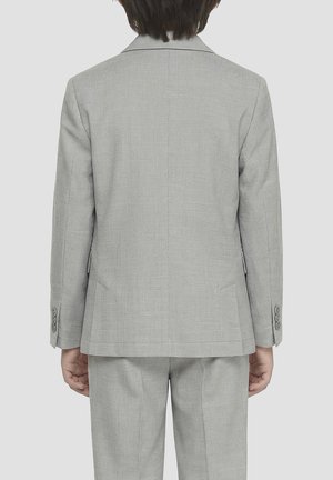 Bambino che indossa un abito grigio chiaro con giacca e pantaloni, mostrato di spalle su uno sfondo uniforme.