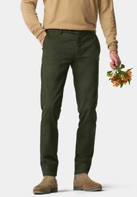 Donkergroene broek met een gladde textuur, slim fit, zijzakken en een knoopsluiting, gecombineerd met beige schoenen en een bloemenboeket.