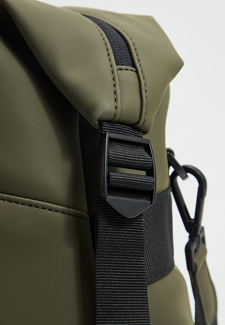 Nahaufnahme eines olivgrünen wasserdichten Rucksacks mit Rolltop-Verschluss, schwarzem verstellbarem Riemen und Kunststoffschnallen.
