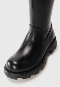Botine negre din piele, cu vârful rotund, talpă groasă și fundație texturată în contrast. Detalii de cusătură vizibile pe lateral.
