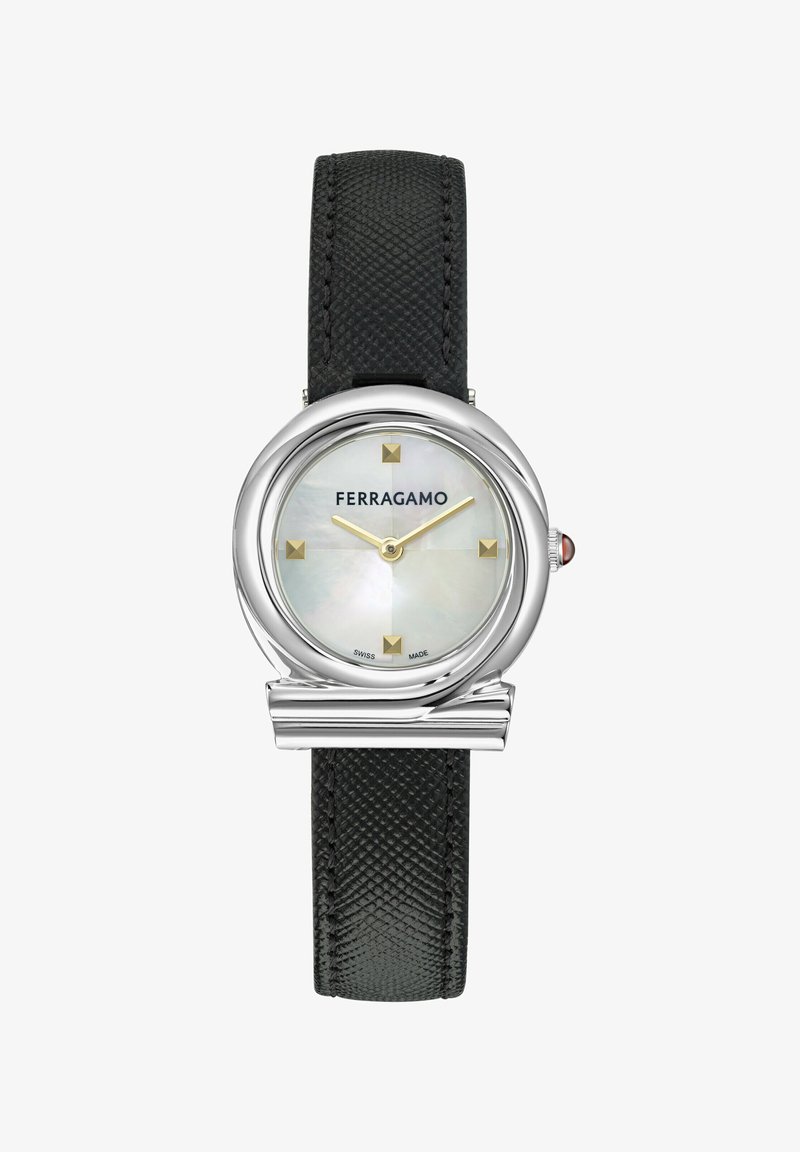 Hõbedane kell ümmarguse pärlivalge detailsusega, kuldsed tunni markerid ja must tekstuuriga nahkrihm. Funktsioneerib Ferragamo brändinguga.