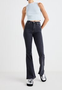 Top corto de color azul claro con cuello alto, combinado con jeans acampanados de lavado oscuro. Zapatos de plataforma plateados y brillantes complementan el atuendo.