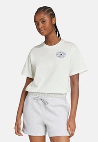 Light beige cotton t-shirt with short sleeves, featuring a blue and white printed logo on the chest. Paired with gray fleece shorts.