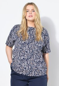 Modrá košile s krátkými rukávy, zdobená bílým vzorem paisley. Měkká tkanina s uvolněným střihém, kulatým výstřihem a postranními rozparky.