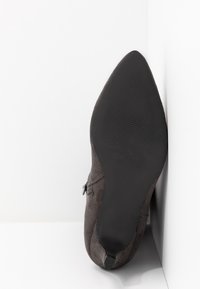 Zapato de ante gris con punta afilada y suela de goma negra lisa. Presenta un detalle de cremallera en el lateral y una textura suave.