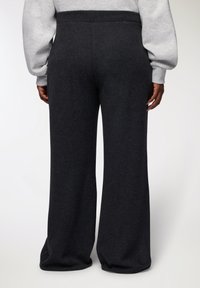 Pantaloni a gamba larga grigio scuro realizzati in tessuto morbido. Presentano una vita liscia e un design pulito e semplice, senza accessori visibili.