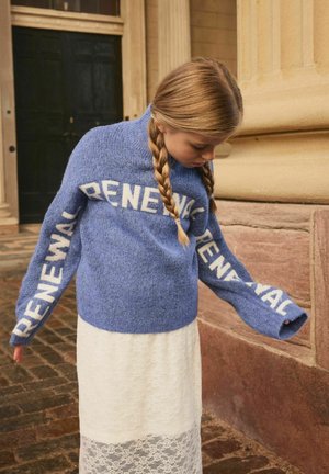 Blå stickad tröja med "RENEWAL" i vit text på ärmarna, tillsammans med en vit spetskjol. Texturerad tyg och avslappnad passform.