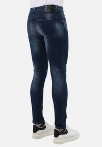 Donkerblauwe skinny jeans met een vervaagde textuur, vijf pockets ontwerp en een zwarte leren merkpatch aan de achterkant van de tailleband.