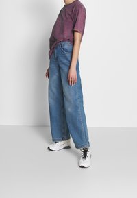 Lösa blå jeans, rosa tie-dye t-shirt och vita sneakers med svarta detaljer. Slätt tyg och avslappnad silhuett.