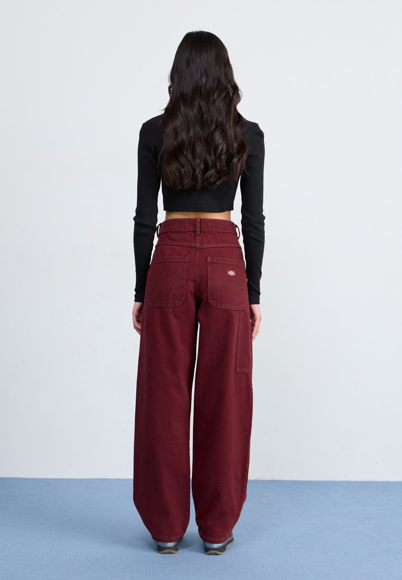 Pantalon bordeaux à jambes larges avec une texture lisse, doté de deux poches arrière et d'un détail de logo. Associé à un haut noir à manches longues ajusté.