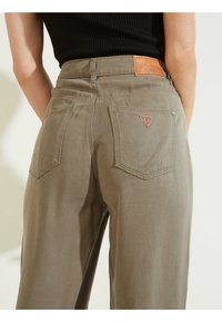 Pantalones de pierna ancha en denim verde oliva apagado, que cuentan con dos bolsillos traseros, un parche de cuero con la marca y un acento de logotipo triangular en el bolsillo derecho.
