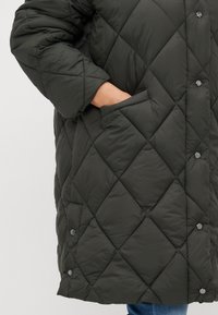 Kvalitetna puffer jakna u tamnozelenoj boji s dijamant uzorkom. Ima bočnu džep i kopčanje na dugmadi. Mekana, teksturirana tkanina.