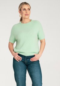 Jasnozielony sweter krótkim rękawem wykonany z miękkiego, puszystego materiału, połączony z ciemnoniebieskimi dżinsami, z okrągłym dekoltem i luźnym krojem.