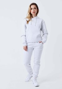 Lichtgrijze sweatshirts en sweatpants set, gemaakt van zachte stof, met een voorzak en trekkoordjes, gecombineerd met witte sportschoenen.