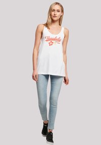 Weißes ärmelloses Tanktop mit roten "Honolulu"-Schriftzug und floralen Grafiken, kombiniert mit hellblauen Skinny-Jeans und schwarzen Turnschuhen.