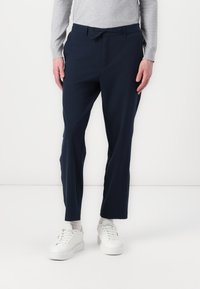Marineblaue Hosen aus einem glatten Stoff, mit einem Kordelzugbund und einer maßgeschneiderten Passform. Kombiniert mit weißen Sneakers.