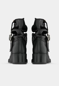 Mustad mustajad nahast ankle saapad, tekstureeritud nahaga, kortsus disain, silmapaistev pandla aktsent ja paks konts. Vaade taga.