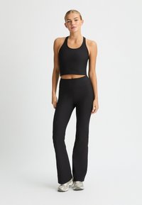 Top corto atlético negro y leggings acampanados hechos de tela elástica, con diseño sin costuras y textura suave. Se llevan zapatillas plateadas.
