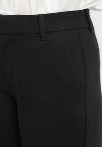 Los pantalones negros cuentan con una tela suave, un diseño ajustado y un frente plano con bolsillos en ángulo. La cintura tiene un cierre discreto.