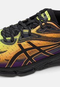 Multi-colored athletic shoe featuring a gradient from yellow to purple, black accents, textured surface, and a distinctive logo on the side.