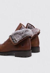 Botas de cuero marrón hasta el tobillo con un cuello de piel sintética gris plegable, puntera redonda y suela de goma texturizada. Presenta ojetes de metal para los cordones.