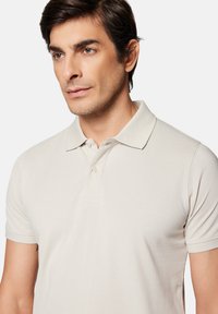 Beżowa koszulka polo wykonana z dzianiny z klasycznym kołnierzykiem, trzyguzikowym zapięciem i krótkimi rękawami. Teksturowana powierzchnia z subtelnymi detalami.