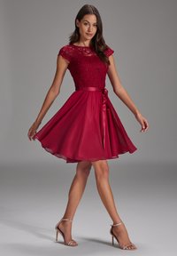 Robe rouge avec un corsage en dentelle, des manches courtes et une jupe en satin évasée. Fini avec une ceinture en satin et un ourlet mi-long.