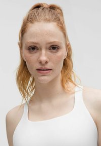 Balta liemenėlė su plačiomis petnešėlėmis, turinti kvadratinį iškirpimą. Modelis turi šviesiai raudonus plaukus ir strazdanas, fone yra neutrali aplinka.