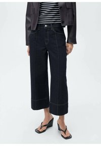 Mørke denim culotter med brede ben, kontrasterende gule stikninger, høj talje-design og forlommer. Båret med en stribet top og hælhøje sandaler.