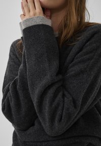 Dunkelgrauer Pullover aus weichem, strukturiertem Stoff, mit kontrastierenden hellgrauen Rippstrickbündchen und lockerem Sitz an den Ärmeln.