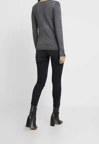 Pull gris à manches longues avec ourlet côtelé, associé à un jean skinny noir. Le mannequin porte des bottines noires à talons avec un design élégant.