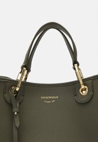 Oliivroheline käekott, mis on valmistatud tekstuurilisest nahast, millel on kuldne riistvara, kahekordsed käepidemed ja kuldne esitlogoga emasdatu ees.