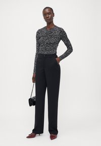 Haut à manches longues noir avec des taches blanches, pantalon noir ajusté, chaussures à talons bordeaux et un petit sac à main noir. Textures lisses.