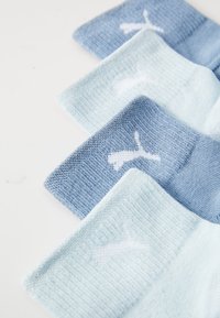 Set med fyra strumpor i olika nyanser av blått, med en mjuk stickad textur och en vit logotypdetalj på mudden.