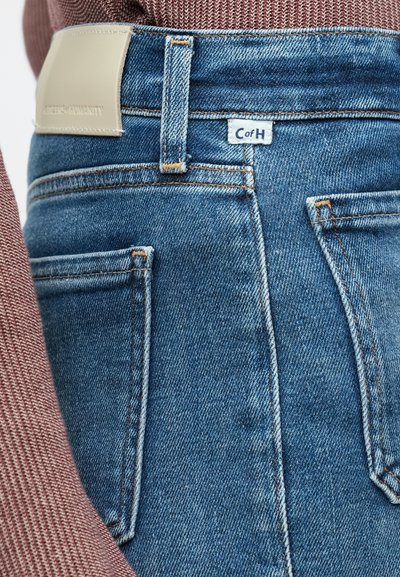 Φθαρμένα τζιν μπλέ από τζιν υλικό με ψηλή μέση και αντίθετη πορτοκαλί ραφή. Διαθέτουν καφέ δερμάτινη ετικέτα και δύο πίσω τσέπες.