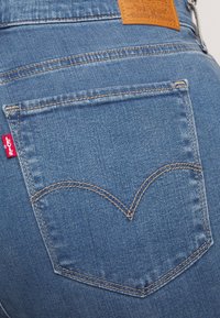 Gros plan sur la poche arrière d’un jean en denim bleu avec des surpiqûres orange et une étiquette rouge Levi's sur le côté gauche.
