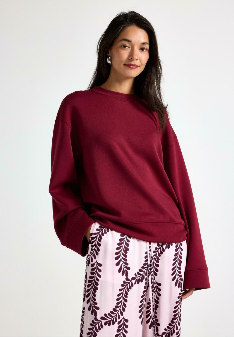 Bordeaux oversized sweatshirt med dropped shoulders, kombineret med lyserøde bukser med mørk lilla bladmønstre.