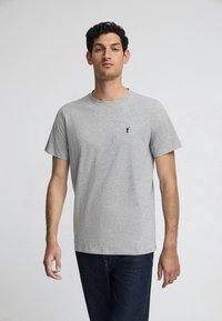 Grijze katoenen t-shirt met korte mouwen, ronde hals en een klein zwart logo op de linkerborst. Soepele textuur en casual pasvorm.