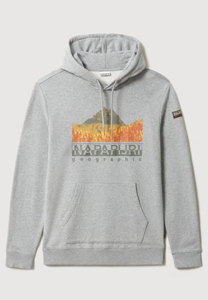 Personne portant un sweat à capuche gris avec un motif de montagne, un pantalon noir texturé avec des patchs, des bottes noires et un sac à dos noir.